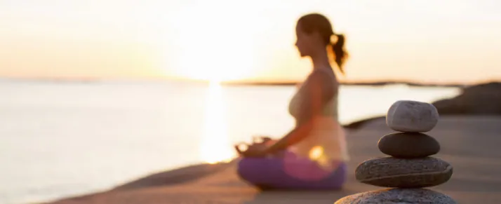 Woman meditating beside calm water at sunrise