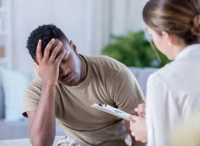 Man holding his head in pain while speaking with a practitioner
