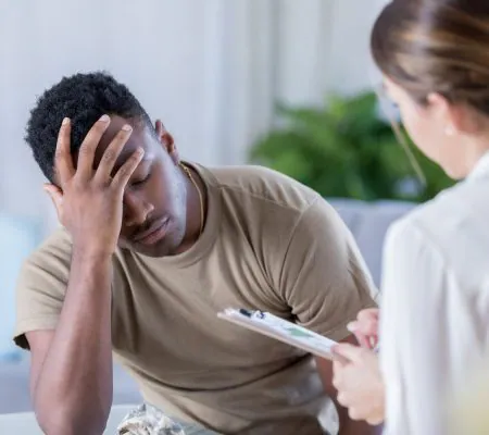 Man holding his head in pain while speaking with a practitioner